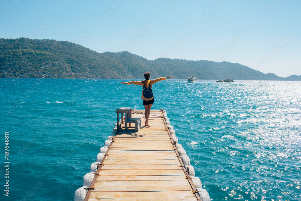 tourist, happy girl with backpack standing on a sea pier breathing fresh air raising hands enjoying the view. Pier, the Turkish city of Simena