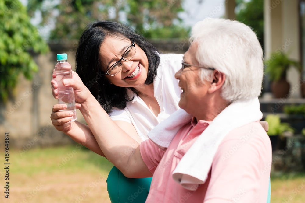 Careful senior woman giving a bottle of water to her partner outdoors in a summer day Careful senior woman giving a bottle of water to her partner outdoors in a summer day