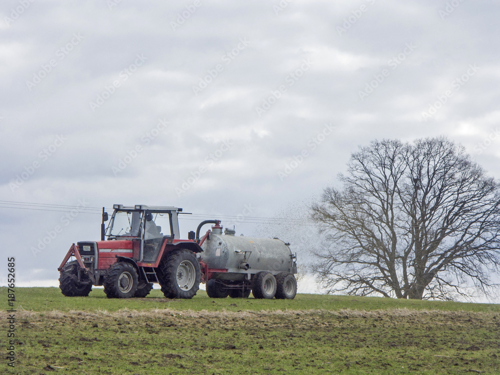 Fototapeta premium Traktor mit Jauchefass - Bauer düngt Wiese