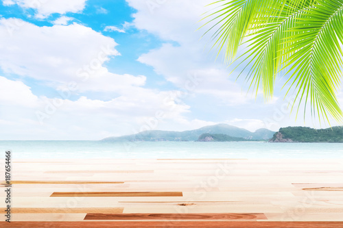 Empty wooden table and palm leaves with party on beach blurred background in summer time. © Akura Yochi