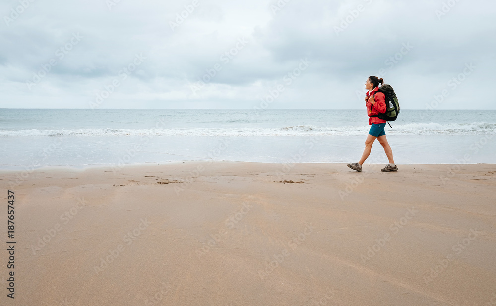 Woman traveler walk on empty ocean beach in rainy day