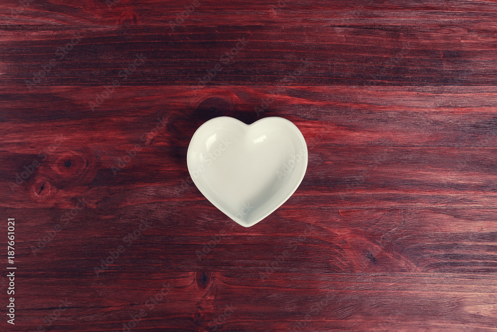 Empty ceramic saucer in the form of heart on a dark wooden table Empty ceramic saucer in the form of heart on a dark wooden table