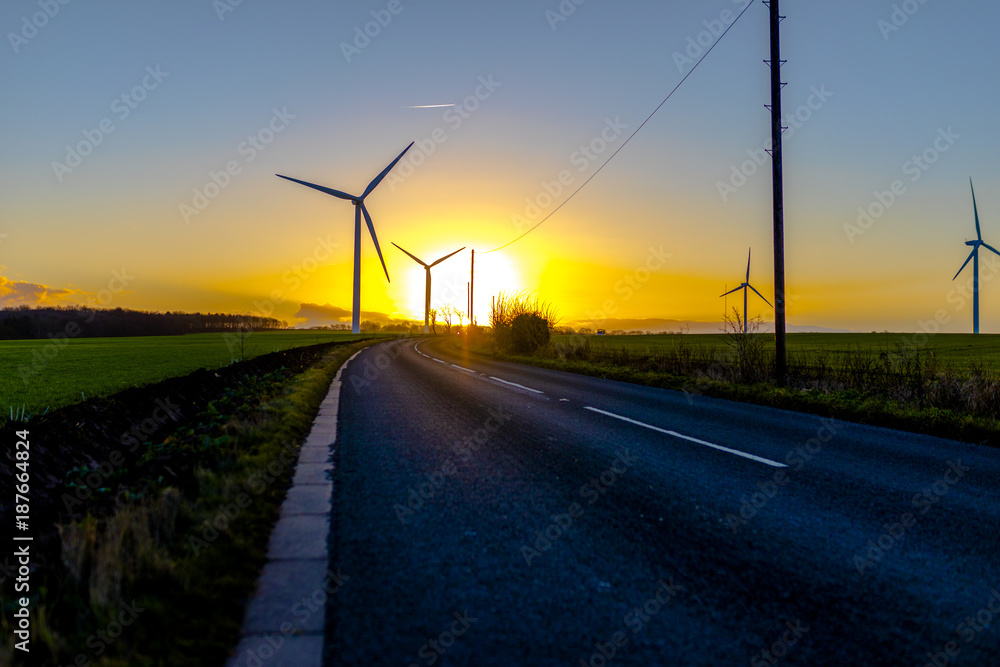 Country road leading to turbines in a field in the UK at sunset or sunrise against a clear winter sky