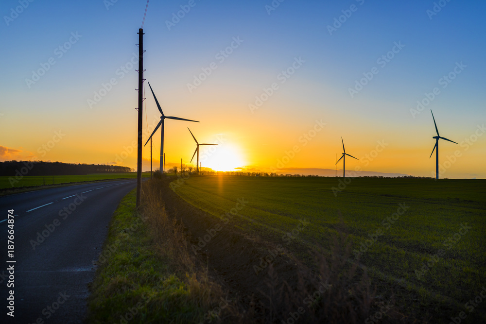 Obraz premium Country road leading to wind turbines in a field in the UK at sunset or sunrise against a clear winter sky
