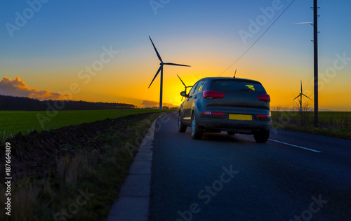 Car driving down country road towards wind turbines in a field in the UK at sunset or sunrise on  a clear winter day photo