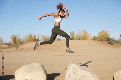 Pretty athletic woman jumping from rocks in mid air photo