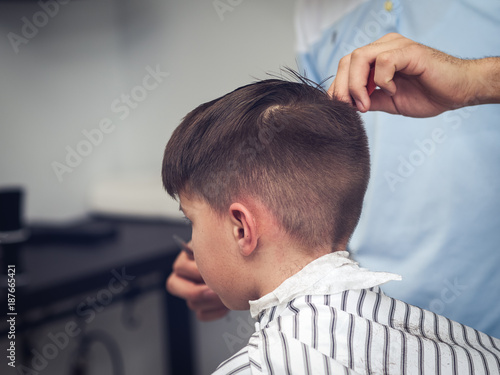 Boy getting haircut by hairdresser in barbershop.