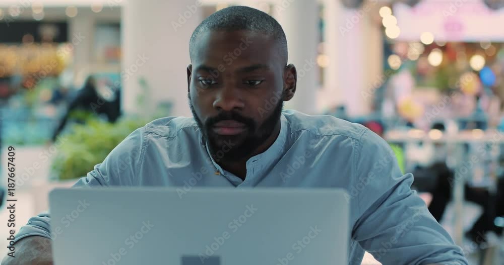 Portrait seriouse african american young man use laptop in cafe concentrated in mall computer web person shopping internet close up technology black business attractive guy sitting slow motion Portrait seriouse african american young man use laptop in cafe concentrated in mall computer web person shopping internet close up technology black business attractive guy sitting slow motion