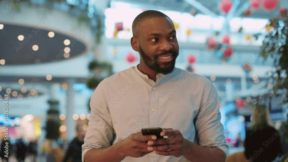 Smiling african american young man using phone in shopping center feel happy christmas happiness internet face technology portrait close up black telephone close up cute mobile holding slow motion Smiling african american young man using phone in shopping center feel happy christmas happiness internet face technology portrait close up black telephone close up cute mobile holding slow motion