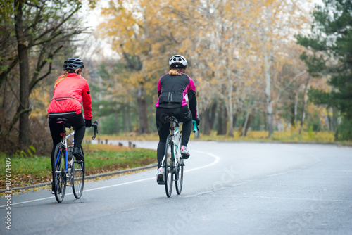 Two Young Female Cyclists Riding Road Bicycles in the Park in the Cold Autumn Morning. Healthy Lifestyle.