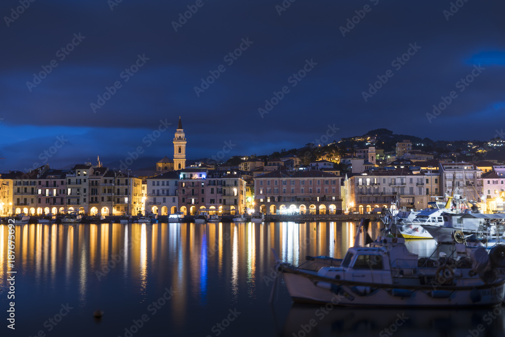 Night view of Oneglia, Imperia. Typical village of the Ligurian coast, Italy, mediterranean sea, with fishing and pleasure boats moored in the harbor.