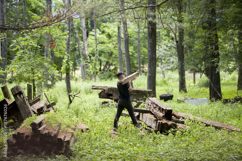 Rear view of boy carrying wood while walking on field in forest Rear view of boy carrying wood while walking on field in forest
