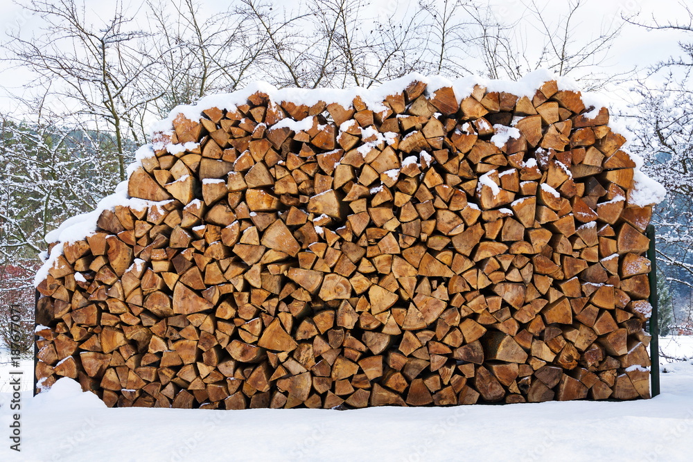 Beautiful stack of chopped firewood in snowy country, sunny winter day