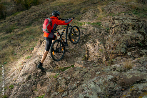 Cyclist in Red Picking the Bike up on Autumn Rocky Trail. Extreme Sport and Enduro Biking Concept.