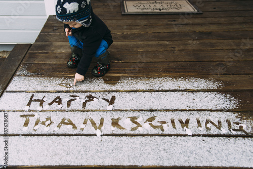 Toddler boy writing thanksgiving text with snow on wooden floor photo