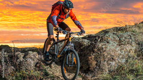 Cyclist in Red Riding the Bike on Autumn Rocky Trail at Sunset. Extreme Sport and Enduro Biking Concept.
