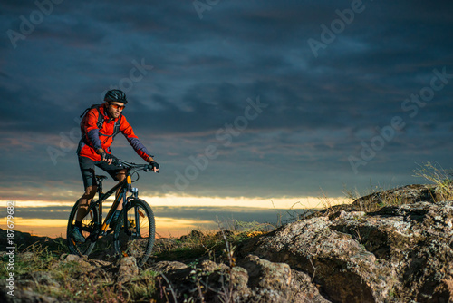 Cyclist in Red Riding the Bike on Autumn Rocky Trail at Sunset. Extreme Sport and Enduro Biking Concept.