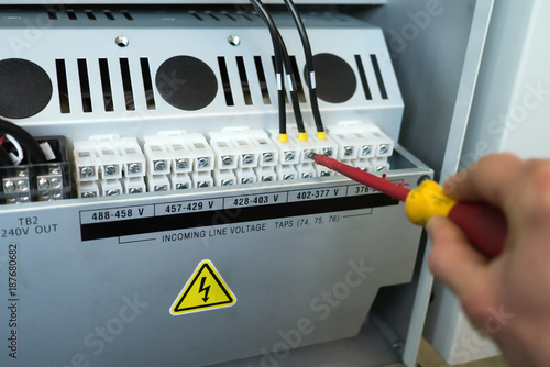 Hand of electrician with screwdriver tighten up electric terminals of transformer in electric cabinet of cnc machine