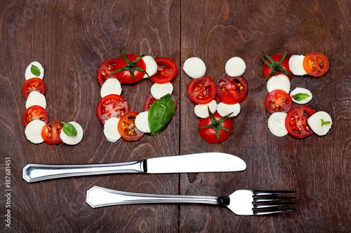 Inscription love of freshness mozzarella, raw tomatoes and basil.Ingredinet s of pizza.Against a dark wooden brown background. Creative valentine day background.Love.Spirit of Italy cuisine photo