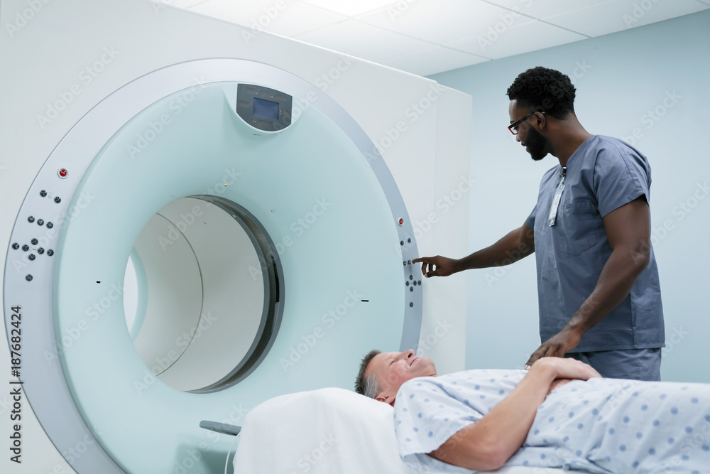 Male nurse adjusting button on MRI Scanner while patient lying in examination room Male nurse adjusting button on MRI Scanner while patient lying in examination room