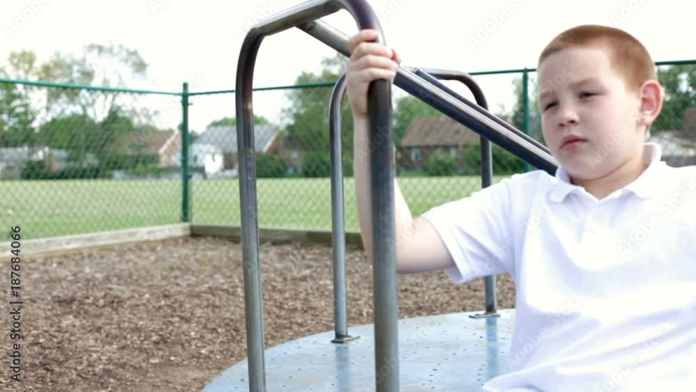 Boy spinning alone on a merry go round in playground.
Boy spinning alone on a merry go round in playground.