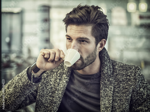 Attractive Man Drinking Coffee while Sitting in a Bar with Serious Expression