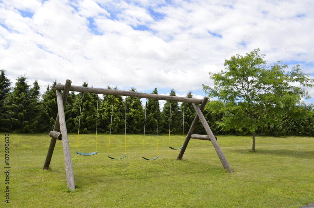 Swing set made of wood timbers in the park on a cloudy summer day