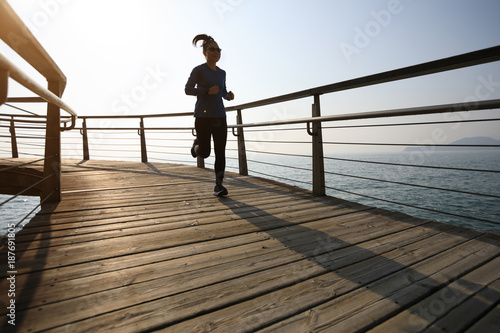 sporty female jogger morning exercise on seaside boardwalk during sunrise © lzf