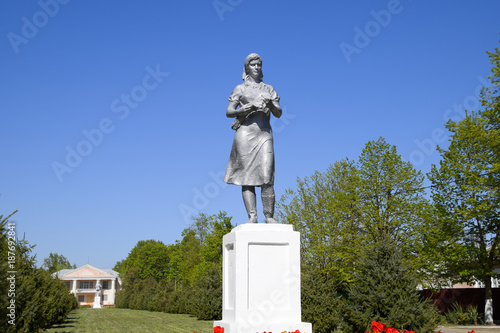 Statue of a collective farmer on a pedestal. The legacy of the Soviet era. A flower bed with tulips and young trees in the village of Oktyabrsky. Krasnodar Krai, Krasnoarmeisky District. photo