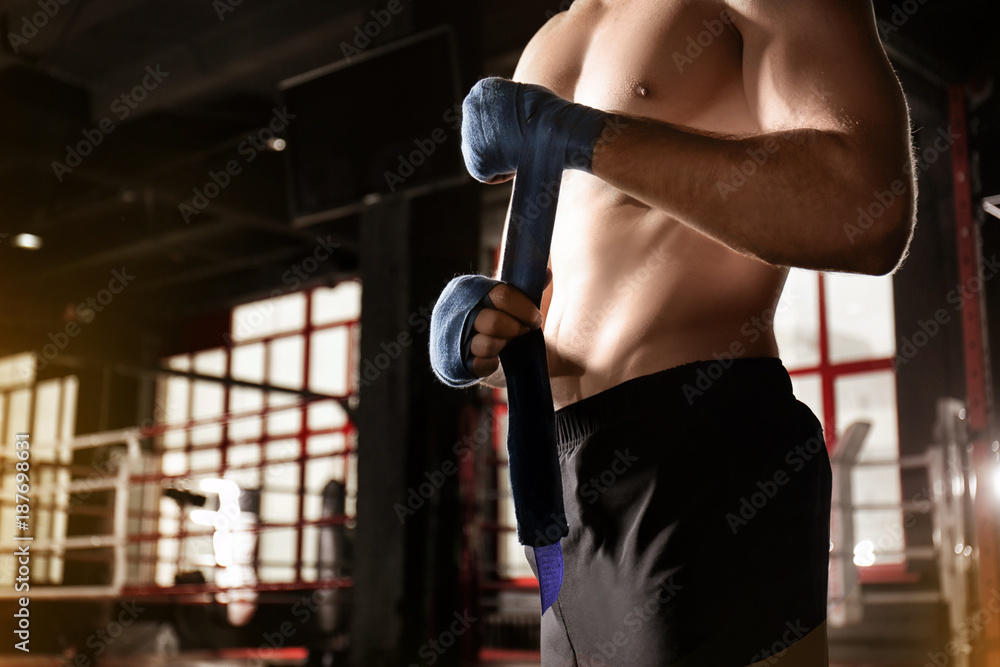 Male boxer applying hand wraps while preparing for training in gym