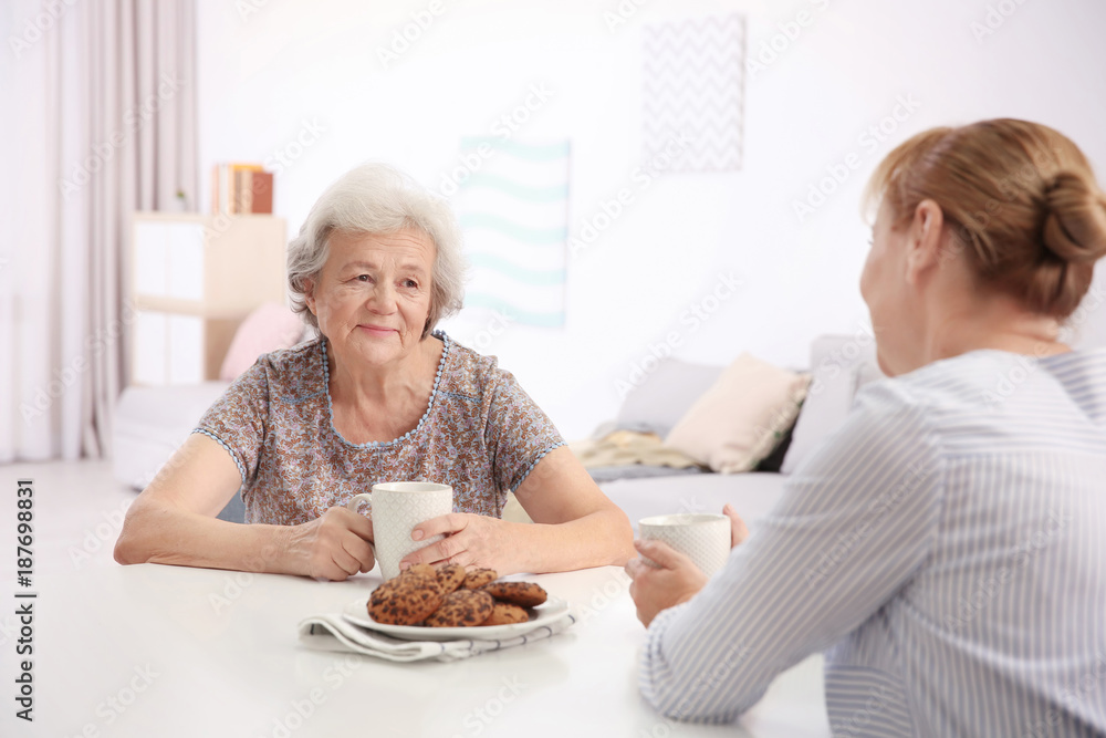 Senior woman and caregiver drinking tea at home