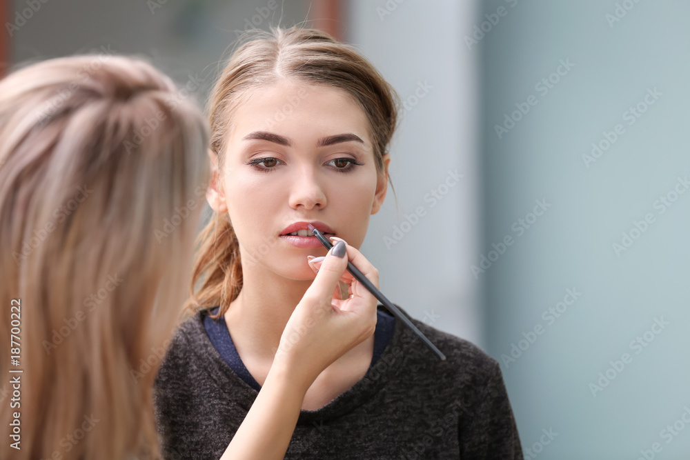 Professional artist creating makeup for beautiful model on blurred background