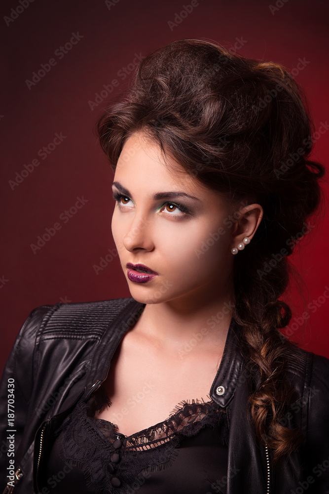 Brunette girl with perfect makeup and stylish hairstyle to look upwards on a dark red background close-up