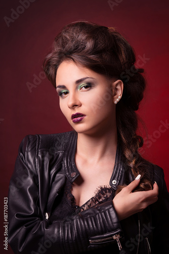Portrait of young brunette woman in stylish manner and in a leather jacket on a dark red background