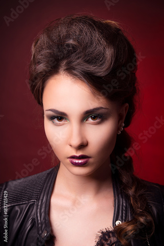 Glamorous portrait of young brunette woman with bright makeup and stylish hair on a dark red background close-up