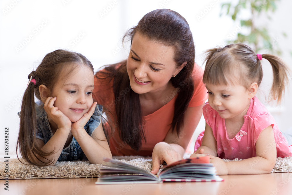 Cute mother and children daughters lie on floor and read book together Cute mother and children daughters lie on floor and read book together