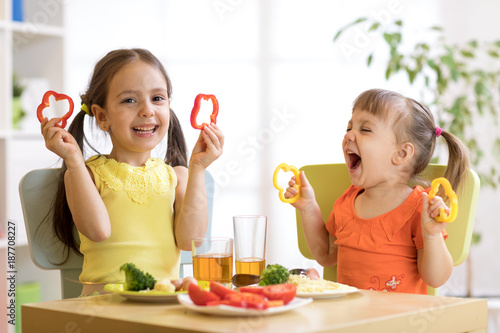 Funny children girls eating healthy food. Kids lunch at home or kindergarten.