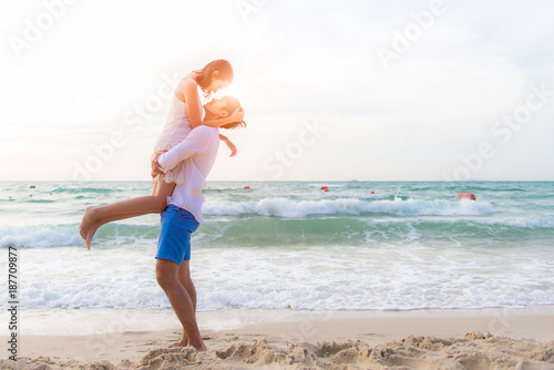 Couple in love. Smiling asian young man is holding girlfriend in his arms on the beach on evening time. Honeymoon relax together on summer travel. Valentine, Travel and Summer Concept.
