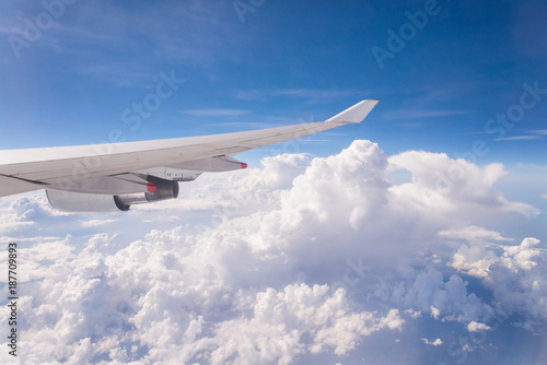 Flying into blue sky and sea of clouds and Wing of airplane with skyline top view as look from window airplane, during flight space for text message, frame or traveling idea concept