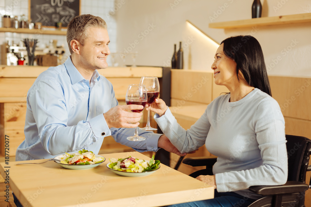 To our love. Handsome gleeful well-built man and a pretty inspired handicapped woman smiling and drinking wine and having dinner To our love. Handsome gleeful well-built man and a pretty inspired handicapped woman smiling and drinking wine and having dinner