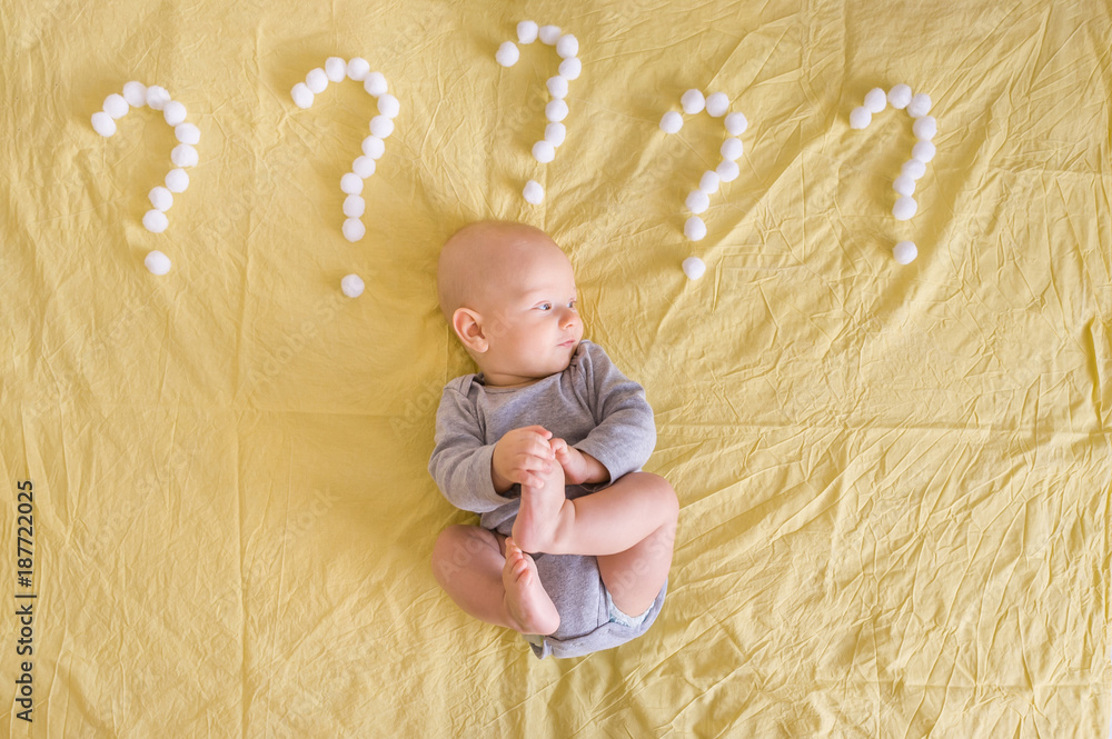 Naklejka premium top view of infant child lying surrounded with question marks made of cotton balls in bed