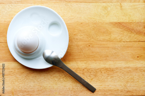 white egg in the plate with the metal spoon on the wooden board