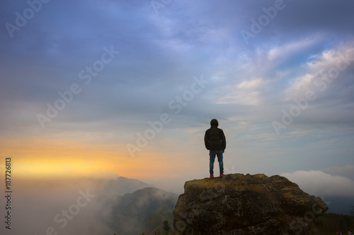 Silhouette traveler man standing on the high rock over the sunrise..