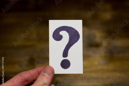 Card with question mark in hand on the background of wooden table