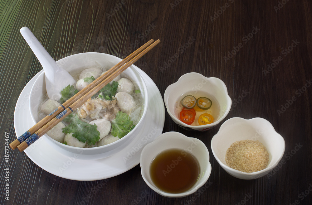 White noodle soup with pork ball in white bowl with seasoning on brown wooden floor thai food White noodle soup with pork ball in white bowl with seasoning on brown wooden floor thai food