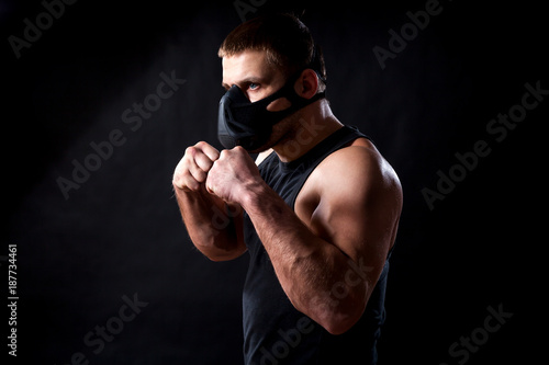 A dark-haired male athlete in a black training mask, a sports shirt is boxed against a black isolated background