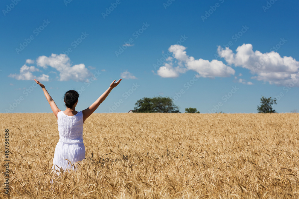 woman in a ripe golden wheat field hugging nature, blue sky with clouds