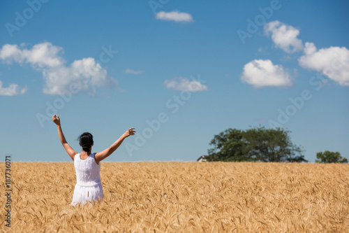 woman in a ripe golden wheat field hugging nature, blue sky with clouds