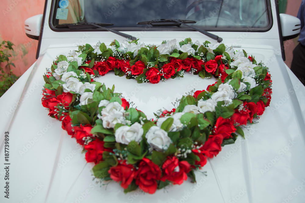 White, red heart bouquet on white bridal car. Wedding car and petals on  top. Luxury wedding car decorated with flowers. Stock Photo