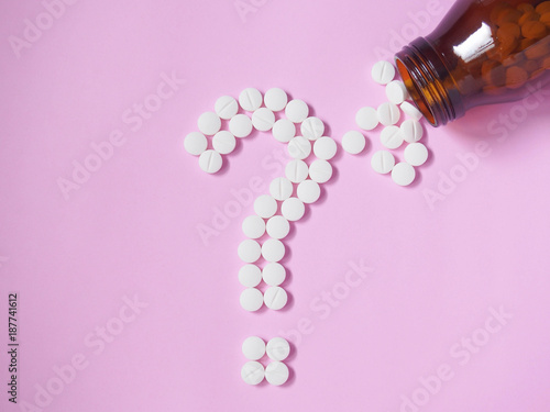 Slika na platnu Question mark made by white pills spilling out of brown glass bottle on pink background